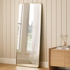 a large mirror sitting on top of a wooden dresser next to a window in a room