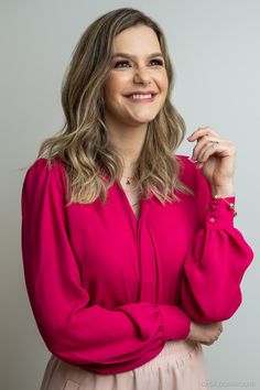 a smiling woman in a pink dress poses for the camera with her hands on her hips