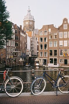 two bikes parked next to each other on the side of a river in front of buildings