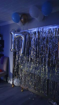 balloons and streamers hang from the ceiling in a room with blue walls, silver curtains and black flooring