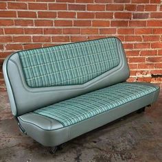 a green leather couch sitting in front of a brick wall with no one on it