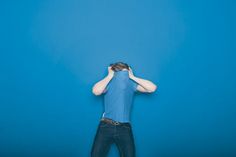 a man standing in front of a blue wall covering his eyes