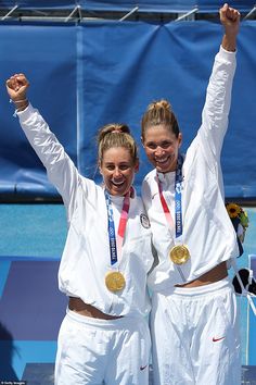 two women standing next to each other on a tennis court holding up their gold medals