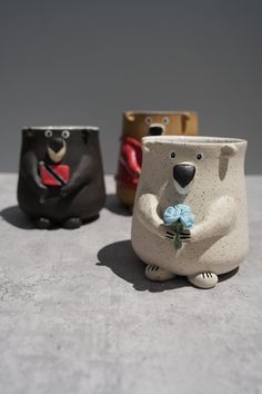 three ceramic bears are holding flowers in their paws and sitting on the concrete surface,