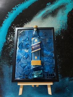 a bottle of blue liquid sitting on top of a wooden easel in front of a painting