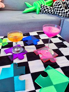 colorful puzzle pieces are sitting on the floor next to two martini glasses and a stuffed animal