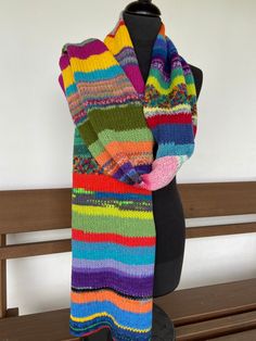 a multicolored knitted scarf sitting on top of a wooden bench