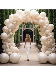 a woman is walking through an archway made out of balloons and white flowers in the background