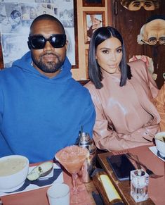 a man and woman sitting at a table with drinks in front of them, posing for the camera