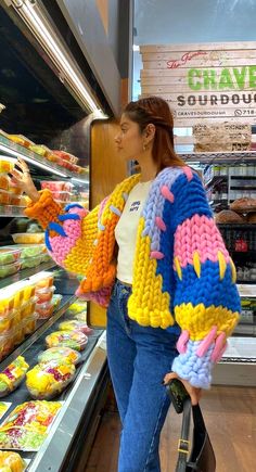 a woman standing in front of a display of crocheted sweaters at a store