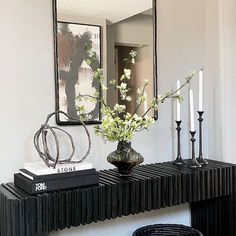 a black console table with flowers and candles on it in front of a framed mirror