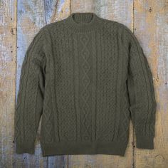 an olive green cable knit sweater hanging on a wooden wall