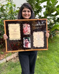 a woman holding up a framed sign with pictures on it in front of some plants