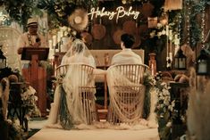 two people sitting on chairs in front of a sign that says happy bday with flowers and greenery