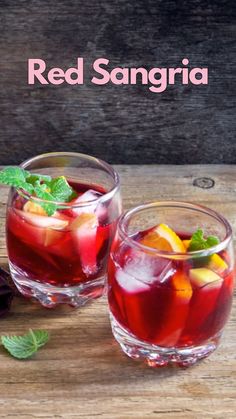 two glasses filled with red sangria and garnished with mint leaves on a wooden table