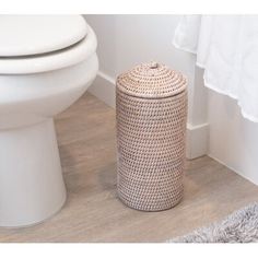 a white toilet sitting next to a trash can on top of a hard wood floor