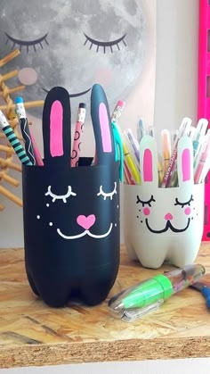 two pencil holders with bunny ears and eyes painted on them, sitting on a desk