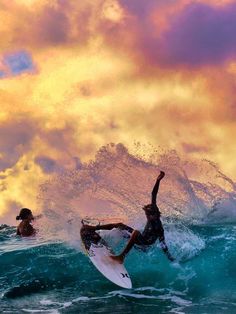 two surfers in the ocean on their surfboards under a colorful sky with clouds