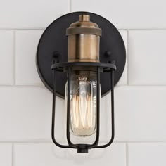 a light fixture on the wall with white tiles in the background and a brick wall behind it