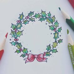 a drawing of a christmas wreath with holly leaves and a bow on it, surrounded by crayon pencils