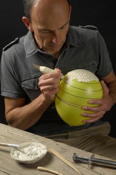 a man is holding a large yellow ball and making something out of it on a wooden table