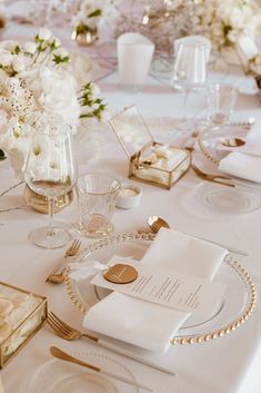 the table is set with white and gold place settings, napkins, and wine glasses