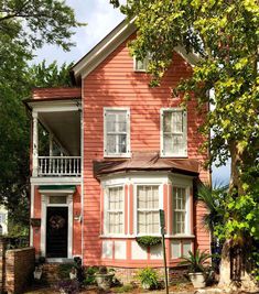 a red house with white trim and windows on the front porch is surrounded by greenery