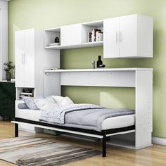 a white bed sitting under a green wall next to a dresser and bookcases