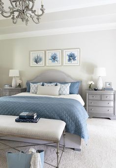 a bedroom with blue and white bedding, chandelier and pictures on the wall