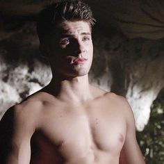 a shirtless young man standing in front of a cave