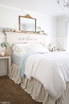 a bed with white sheets and ruffled bedspread in a bedroom next to a chandelier