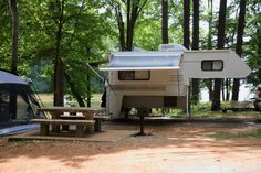 an rv parked in the woods next to a picnic table with a camper on it