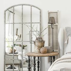 a mirror sitting on top of a bed next to a table with flowers in it