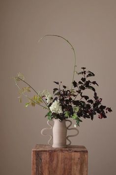 a vase filled with flowers sitting on top of a wooden table next to a wall