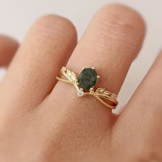 a close up of a person's hand holding a ring with a green stone