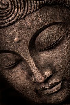 the face of a buddha statue with its eyes closed and one eye closed, in brown tones