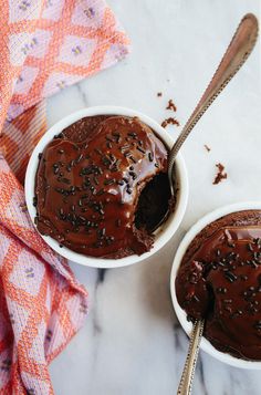 two white bowls filled with chocolate ice cream on top of a marble table next to a spoon