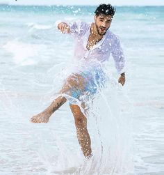 a man in white shirt and blue shorts kicking up water on his feet at the beach