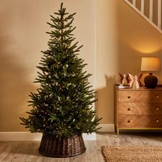 a small christmas tree in a basket next to a stair case with lights on it