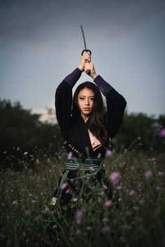 a woman holding two swords over her head while standing in a field full of flowers