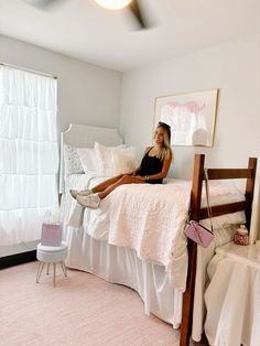 a woman sitting on top of a bed next to a white chair and pink rug