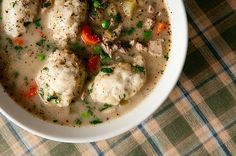 a white bowl filled with meat and vegetable soup on top of a checkered table cloth