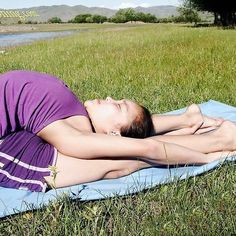 a woman laying on top of a blue towel in the grass next to a river