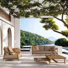 an outdoor living room with white walls and wood furniture, overlooking a pool in the background