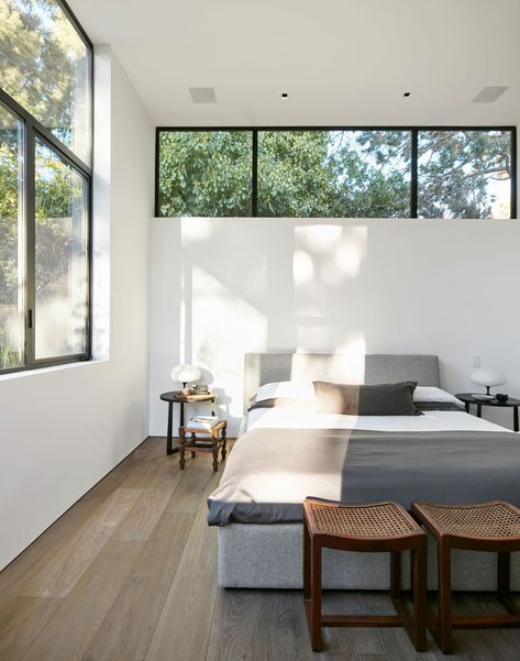 This modern master bedroom has a row of windows above the bed, with a second set of windows adding to the amount of the natural light the room receives. #ModernBedroom #BedroomDesign High Window Above Bed, High Windows In Bedroom, Bedroom High Windows, Bedrooms With Natural Light, Bedrooms With Two Windows, Natural Lighting Bedroom, Windows In Bedroom Ideas, Ceiling Window Bedroom, Bedroom Window Above Bed