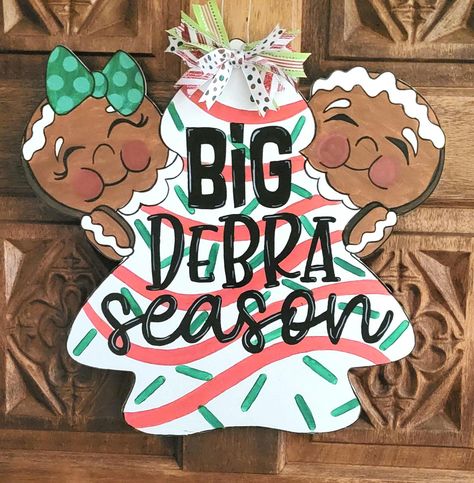 Transform your front door with our whimsical Big Deborah Season wooden door sign. This is hand-painted with a delightful Gingerbread Man design and topped with holiday ribbon that will bring joy and laughter to your festive decor. Perfect for spreading holiday cheer or as a funny gift for friends and family, this large sign is not just a decoration; it's a conversation starter that will make your entrance unforgettable!       - Hand-painted and comes with a wire hanger and ribbon bow on top. Ribbon may be different than shown in picture depending on availability.       - Sprayed with a sealer to make it suitable for outdoor use, but it is highly recommended to hang this  sign out of the direct elements. We are not responsible for any damage caused by rain, wind, sun, hail, snow, etc. Big Deborah, Sign For Door, Custom Door Hangers, Little Debbie, Winter Door, Wooden Door Signs, Funny Gifts For Friends, Large Sign, Hanger Design