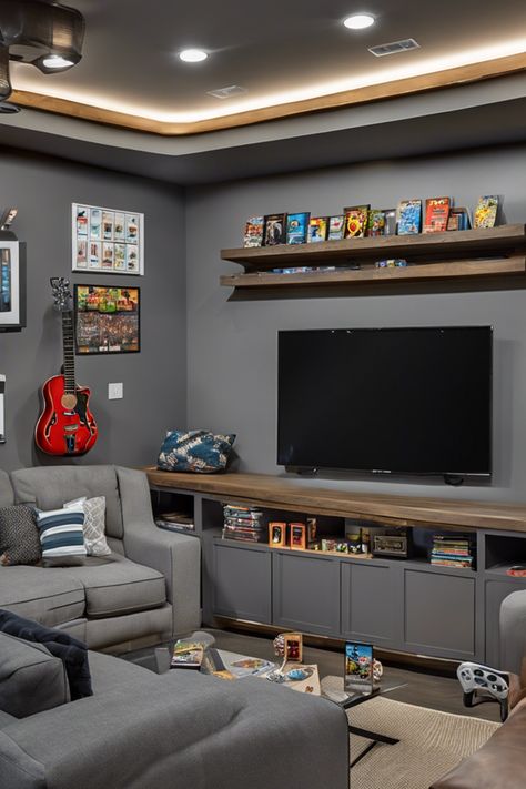 Modern entertainment room with a large TV, shelves holding video games and memorabilia, a red guitar on the wall, and a gray sectional sofa. Loft Gaming Room, Kids Video Game Room, Alternative Formal Dining Room, Gaming Lounge Interior Design, Basement Game Room Ideas Family, Multiple Tv Wall Ideas, Tv Gaming Room, Gamer Living Room Ideas, Kids Gaming Room