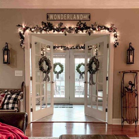 Enter into a winter wonderland through these white French doors decorated with Christmas wreaths. The wreaths are paired with black gingham bows. Black and glass candle sconces flank the double doors...   Image: my.farmhouse.fanatic.life Christmas French Doors, Sliding Door Christmas Decorations, Doorframe Decor Christmas, French Doors Decor Ideas, Christmas Decor Sliding Glass Door, Christmas French Doors Decorations, Christmas Patio Door, French Doors Christmas Decor, French Door Christmas Decor