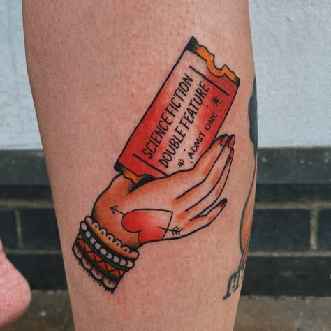 Traditional tattoo of hand holding a red ticket, referencing Rocky Horror. Vhs Tattoo Traditional, Dr Frankenfurter Tattoo, Horror Tattoos Traditional, Horror Movie Inspired Tattoos, American Traditional Movie Tattoo, Rocky Horror Art, Traditional Horror Movie Tattoos, Rocky Horror Tattoo Ideas, Traditional Tattoos Horror