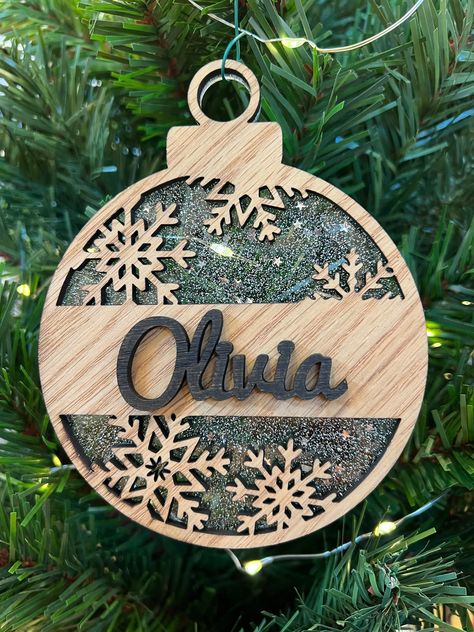 "Laser cut ornaments personalized with a name! These ornaments are cut from oak and acrylic. Choose from standard or speciality acrylics. The speciality acrylics contain accents, such as glitter, to capture the sparkle from your Christmas tree lights! This ornament measures  4\" wide. How to Order -------------- Please include in the checkout notes whether you prefer cursive font or printed font. If not specified, then it will ship with cursive by default. Thank you!" Mdf Christmas Ornaments, Laser Christmas Decorations, Wood Laser Ornaments, Laser Engraving Ornaments, Acrylic Items To Sell, Laser Wood Ornaments, Laser Leather Engraving, Balsa Wood Cricut Projects, Laser Engraving Christmas Ideas